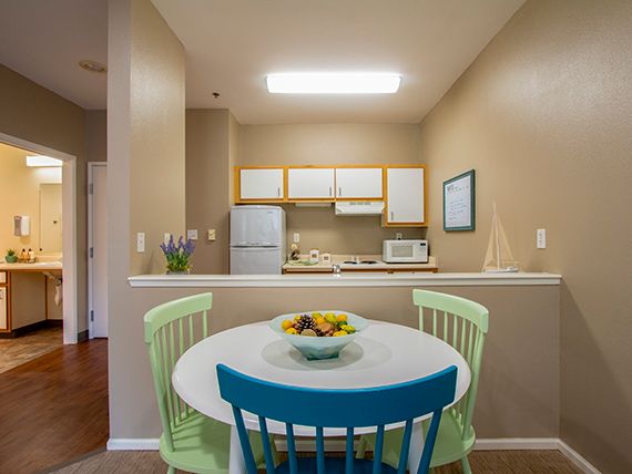 A cozy kitchen and dining area with colorful chairs around a round table, featuring modern appliances in a compact space.