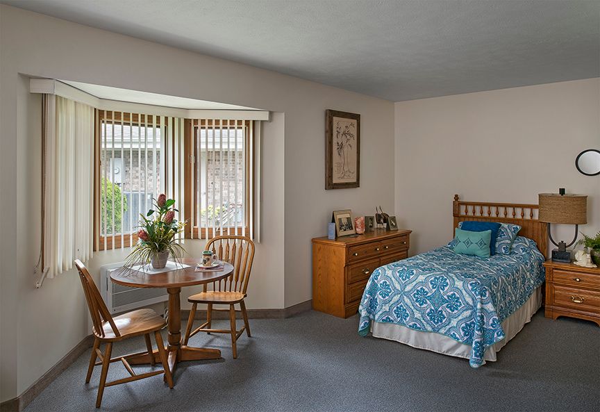 A cozy bedroom with a single bed, wooden furniture, and a small dining set by the window.