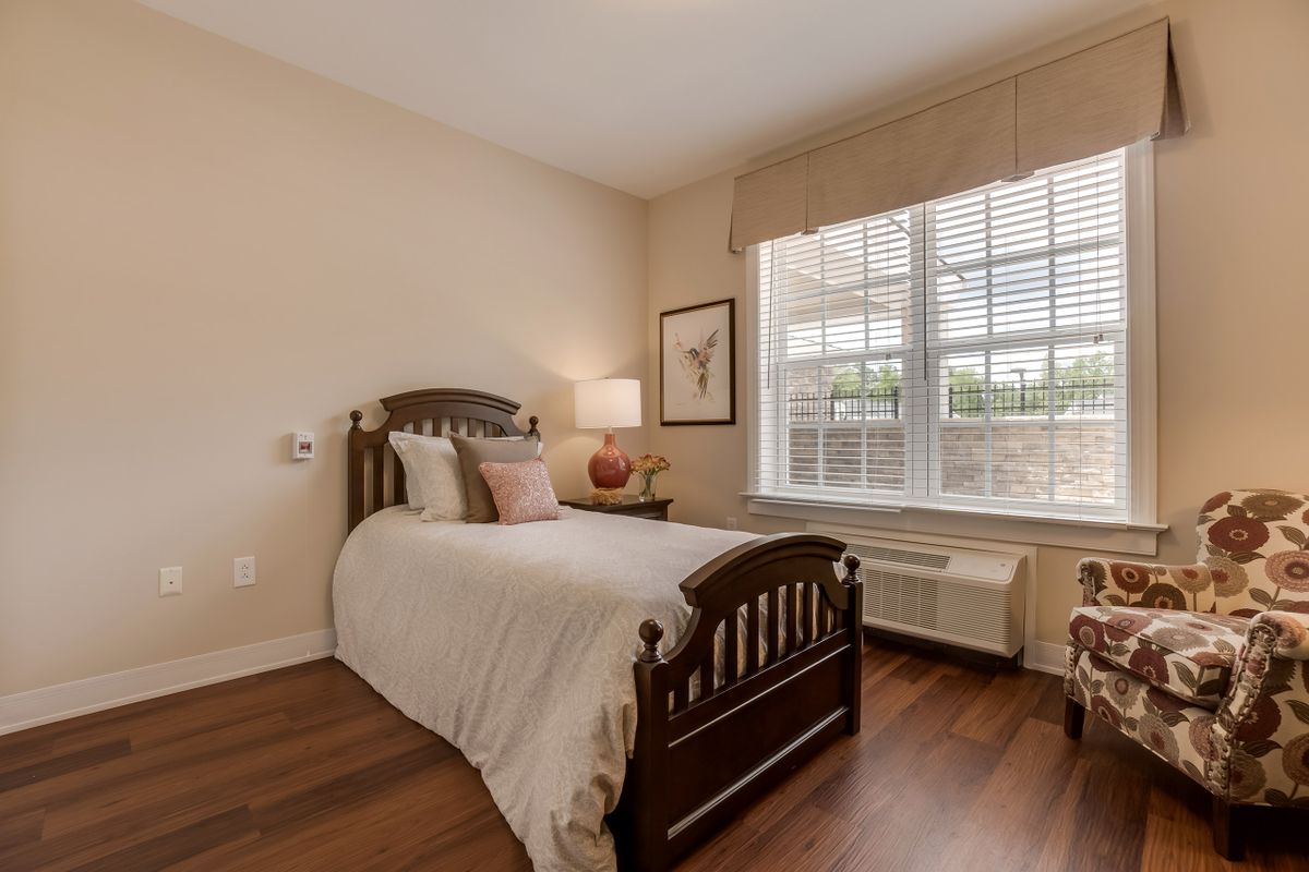 A cozy bedroom with a single bed, wooden furniture, and a large window.