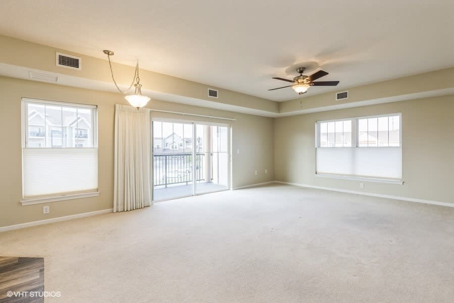 Spacious living room with carpet flooring, ceiling fan, and large windows.