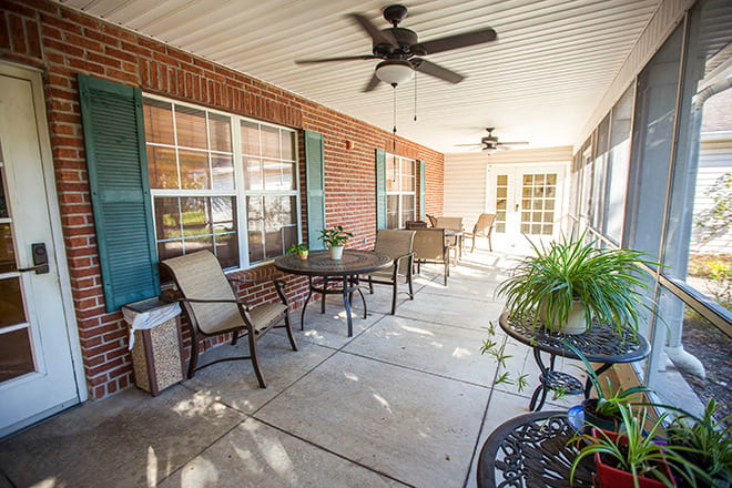 A cozy patio with outdoor furniture, ceiling fans, and potted plants against a brick wall.