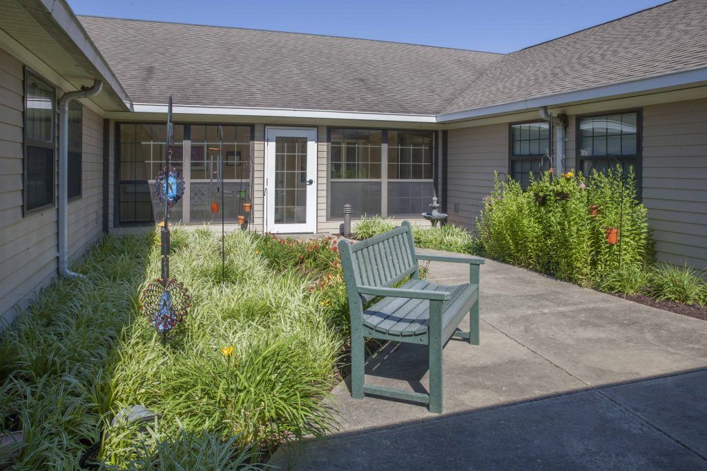 A tranquil garden patio featuring a bench surrounded by lush plants in front of a house.