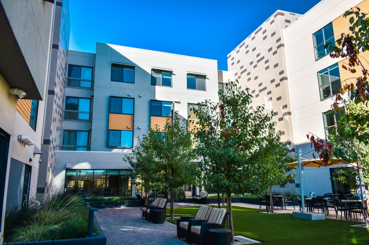 A modern courtyard with benches and trees surrounded by a multi-story building.