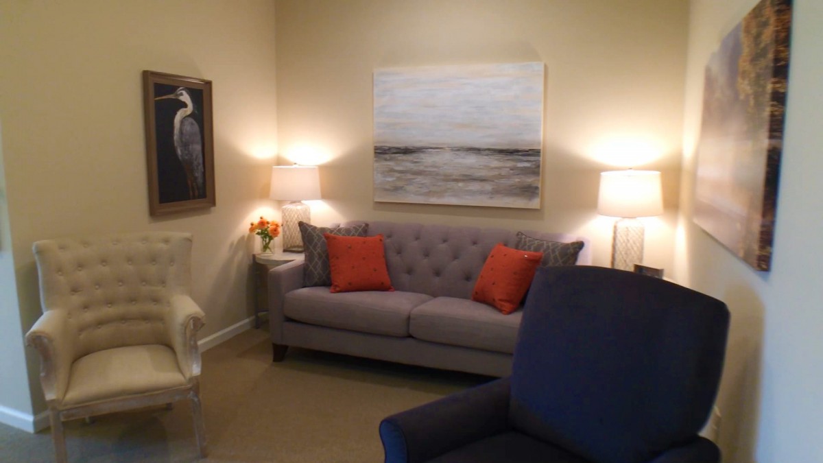 A cozy living room featuring a gray sofa with orange pillows, illuminated by warm lamps and decorated with artwork on the walls.