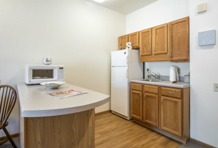 A compact kitchen with wooden cabinets, a refrigerator, and a microwave on the counter.