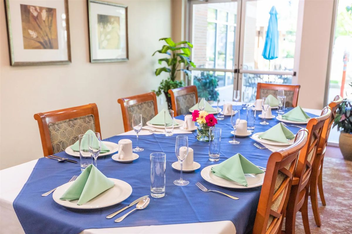 A dining table elegantly set with a blue tablecloth, green folded napkins, floral centerpiece, and neatly arranged cutlery.