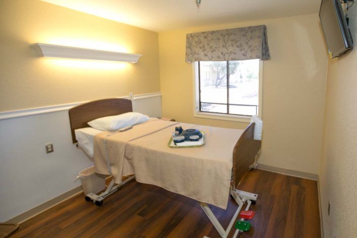 A hospital room with a single bed and a window providing natural light.