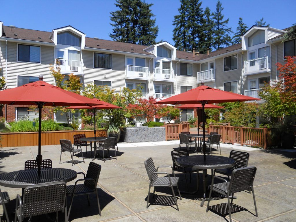 Outdoor courtyard with tables, chairs, and red umbrellas in a residential complex.