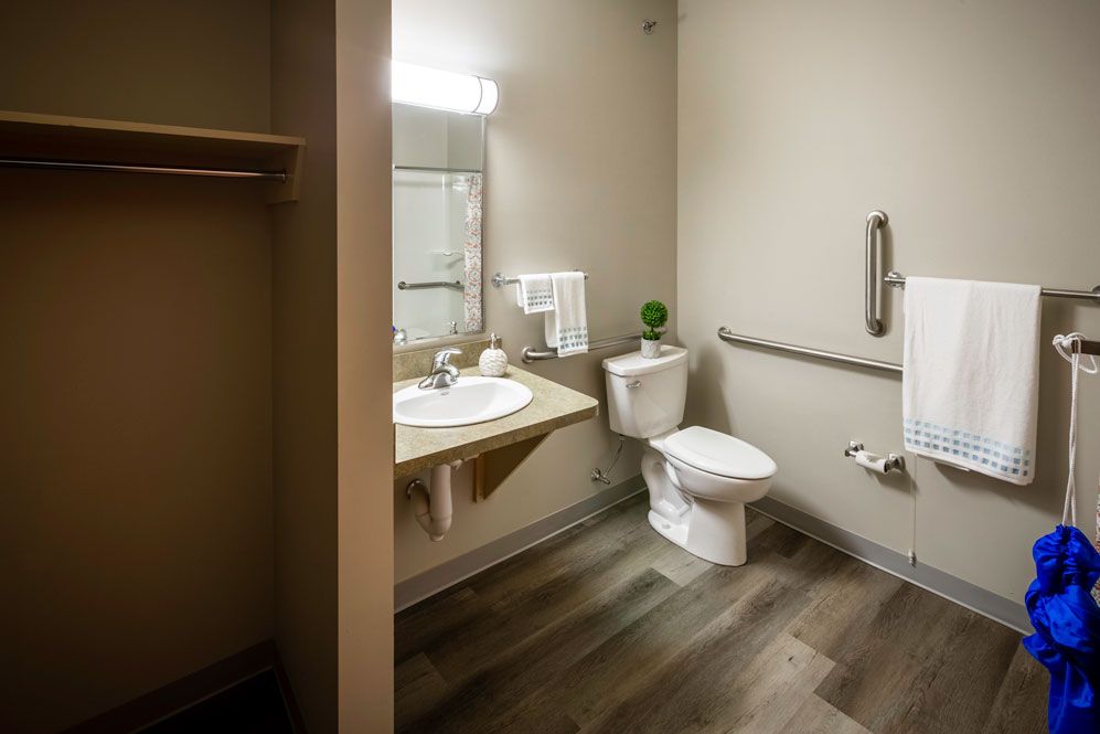 A clean and modern bathroom with a sink, toilet, mirror, and handrail.