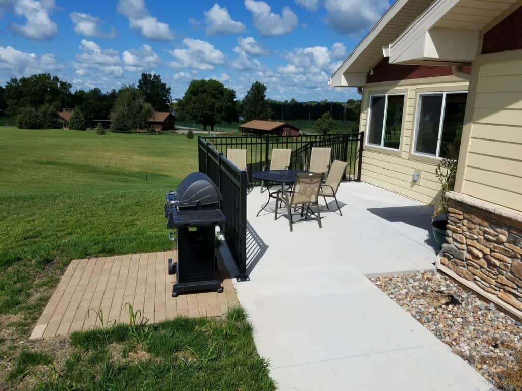 A sunny patio with outdoor seating and a grill, overlooking a spacious backyard.