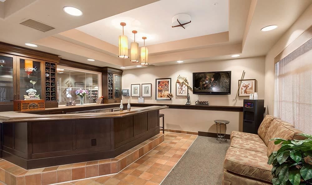 A cozy bar area with a counter, artwork on the walls, and a television.