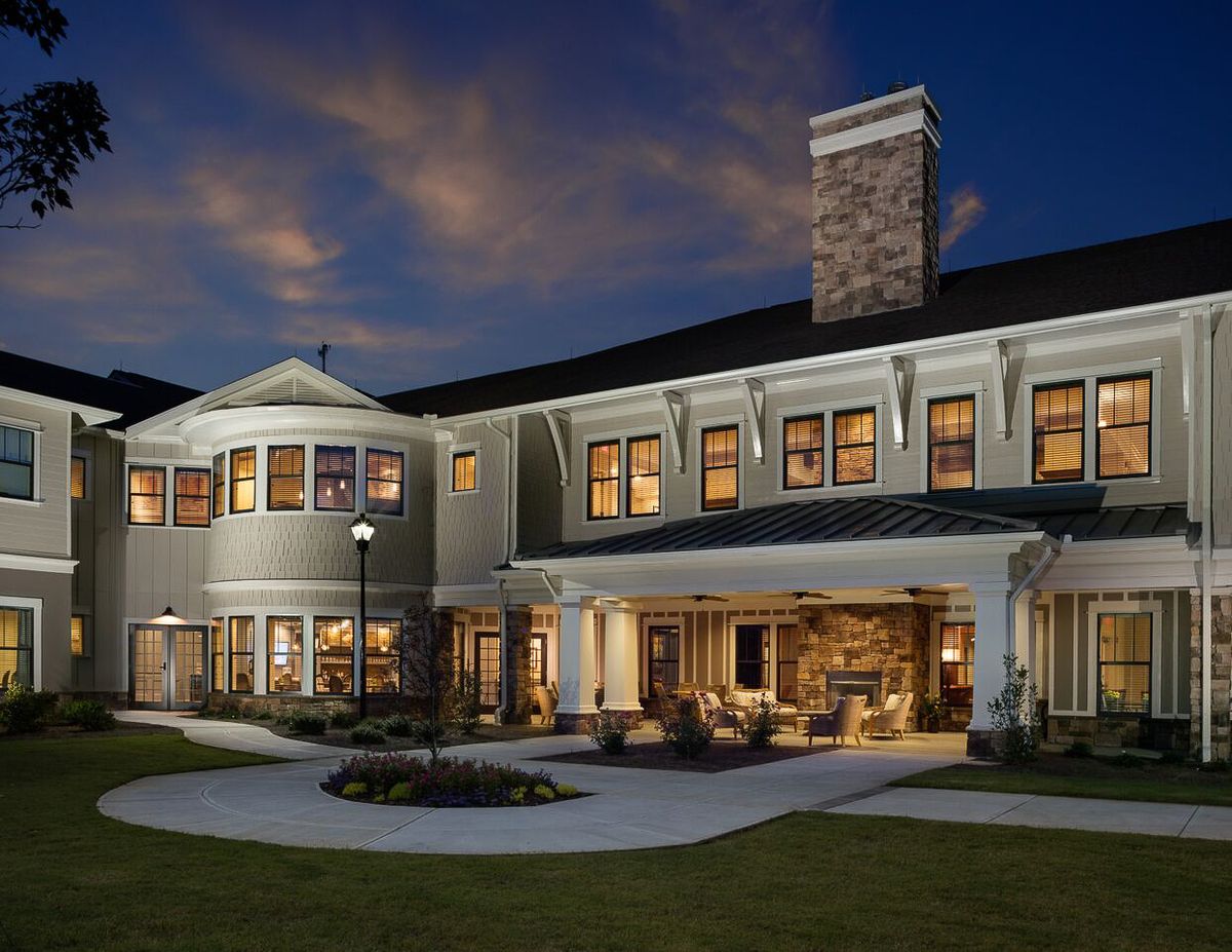 A large, two-story house illuminated at night with a spacious yard and darkening sky.