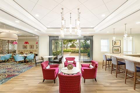 A spacious living room with red chairs, a chandelier, and large windows overlooking a garden.
