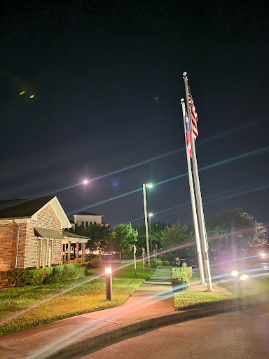 An illuminated American flag stands tall against the night sky, surrounded by well-lit pathways and buildings.