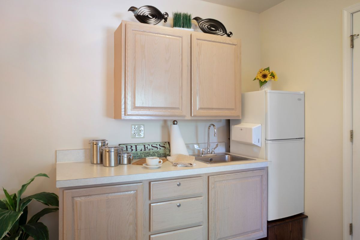A compact kitchen area featuring wooden cabinets, a refrigerator, and countertop storage containers.