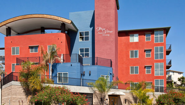 A colorful modern apartment building with red and blue exteriors, surrounded by palm trees.