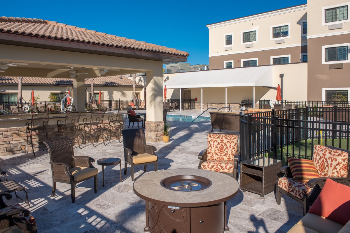 A sunny outdoor patio area at a hotel, featuring comfortable furniture and a fire pit.