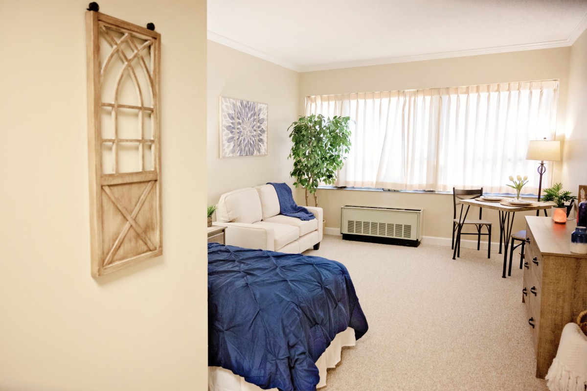 A cozy bedroom with a blue blanket on the bed, decorative elements, and ample natural light.