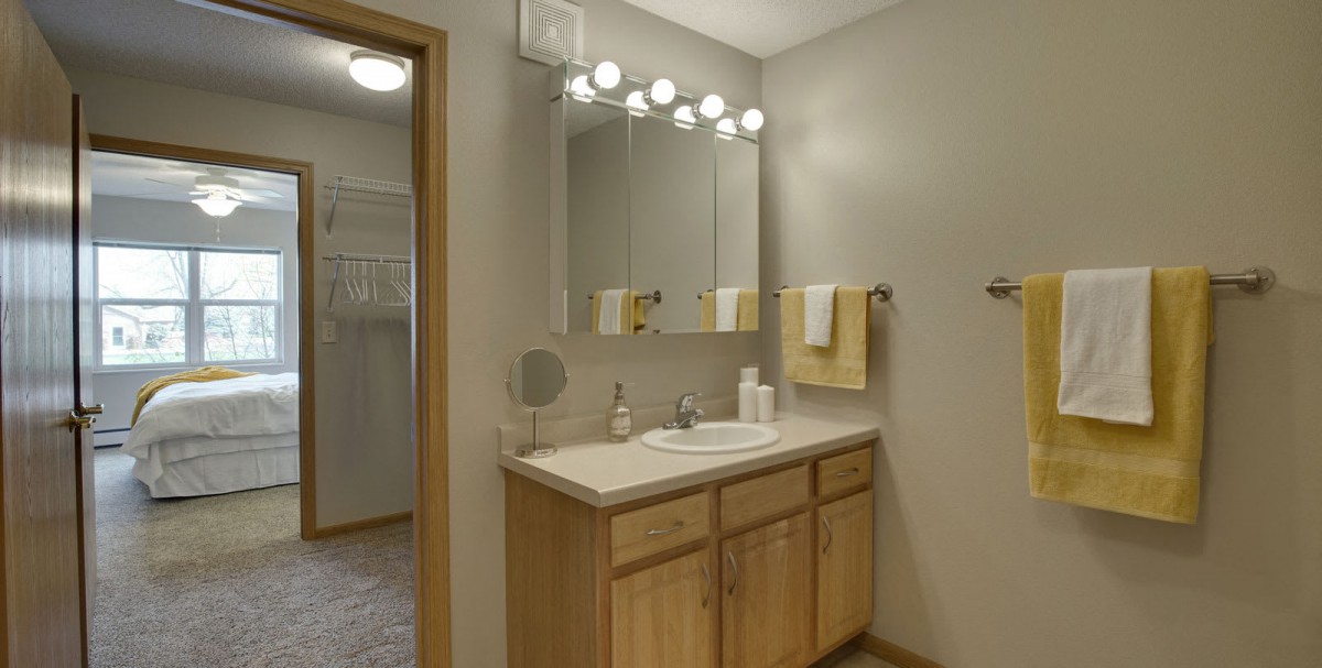 A well-lit bathroom with a wooden vanity and mirror, featuring neatly arranged towels.