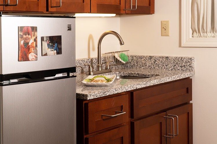A modern kitchen with a stainless steel refrigerator, granite countertop, and wooden cabinets.