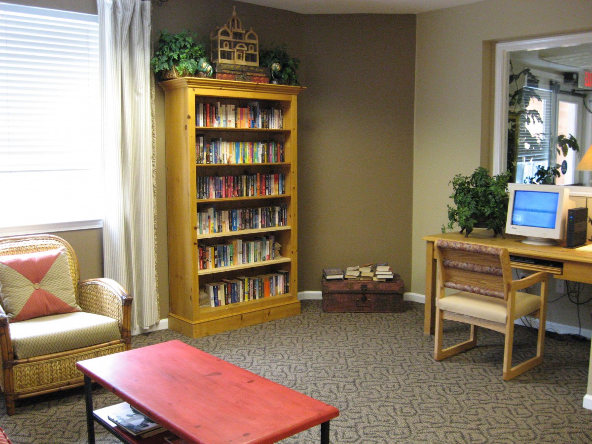A cozy reading room featuring a wooden bookshelf filled with books, a red table, and comfortable chairs.