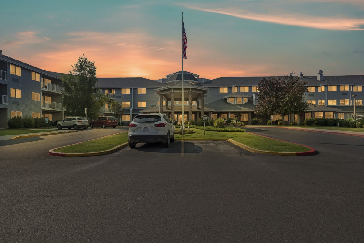 A building with a flag in front, seen at sunset with a car parked in the driveway.