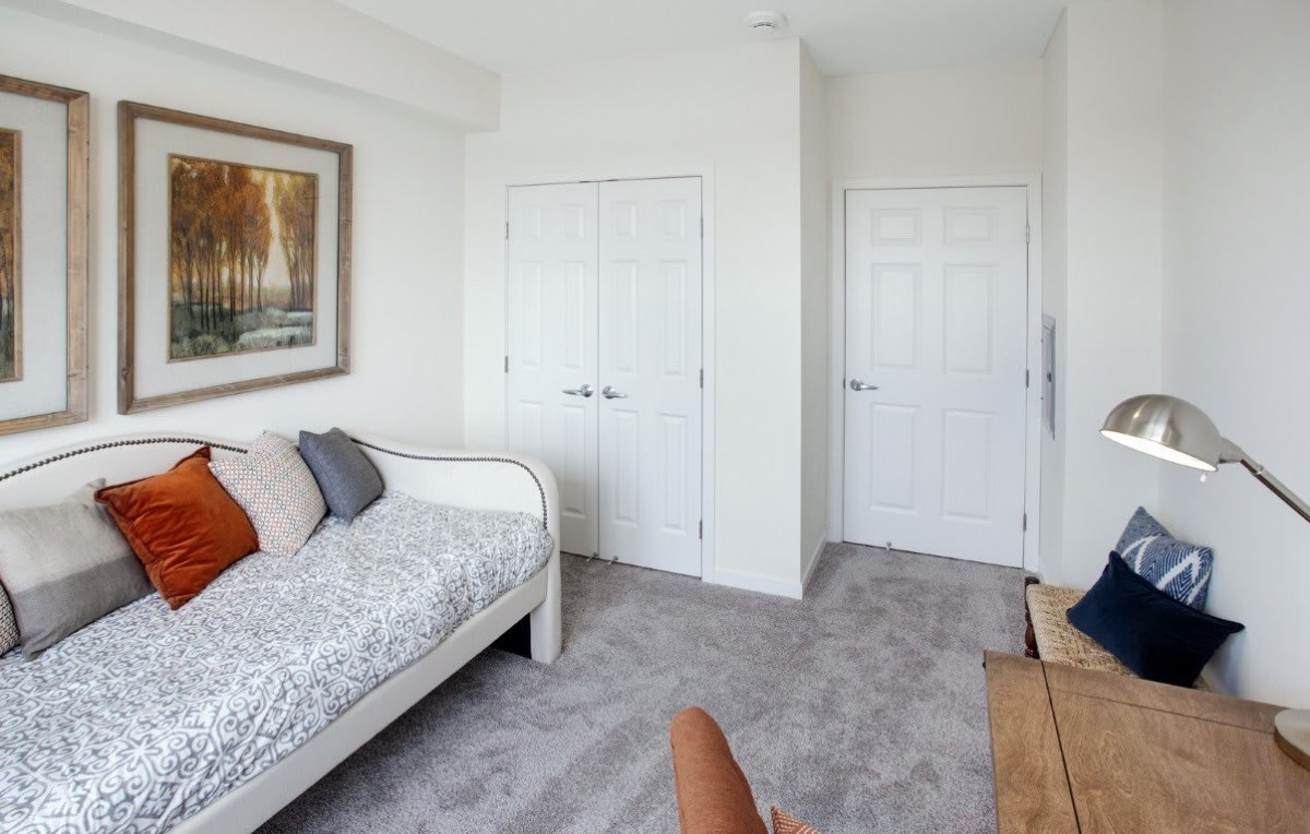 A minimalist bedroom with a daybed, white walls, and soft carpet flooring, conveying a cozy atmosphere.