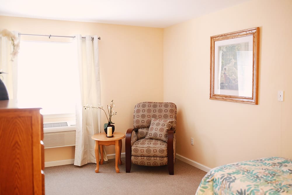 A cozy living room corner with a patterned chair, small wooden table, and window curtains.