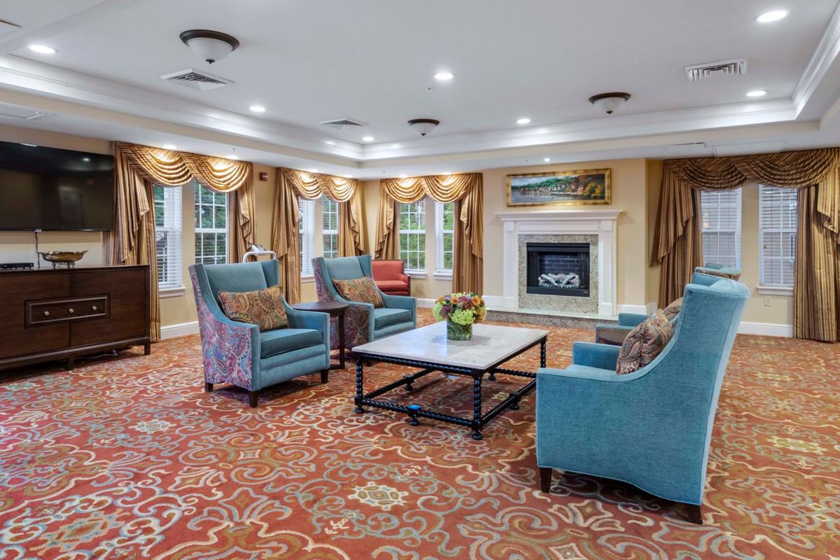 A cozy and elegant living room with blue armchairs, a fireplace, and ornate carpeting.