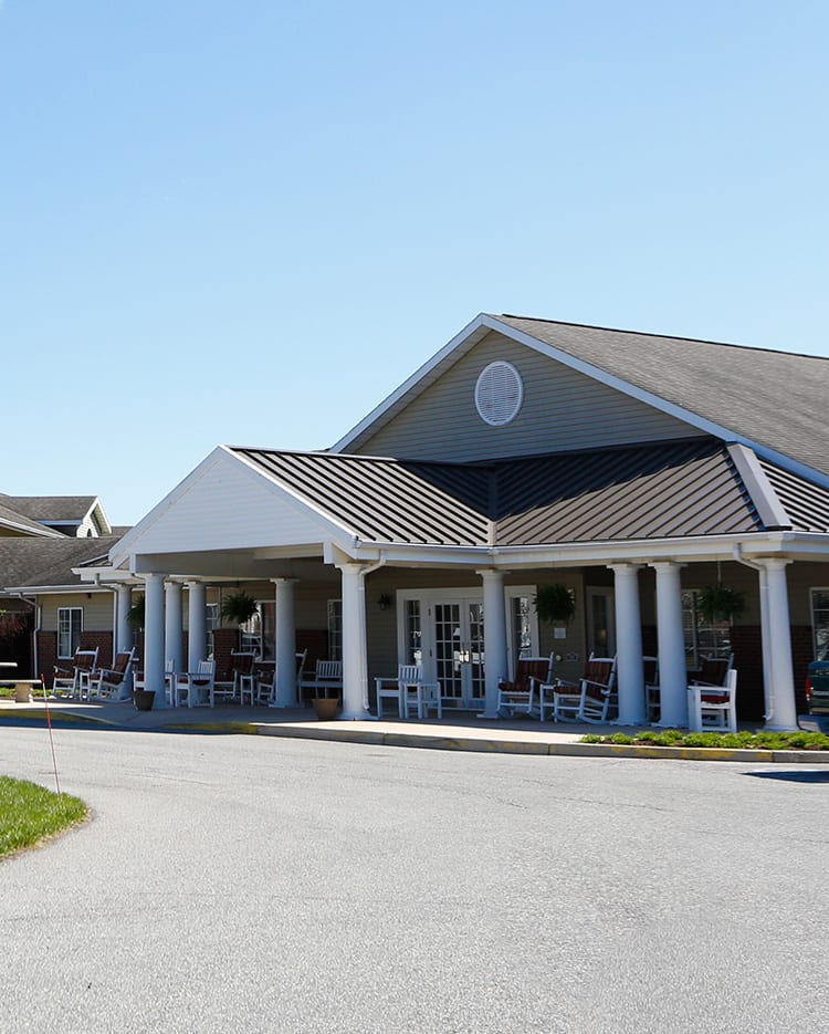 A large building with a porch and columns, featuring a gabled roof, captured on a clear day.