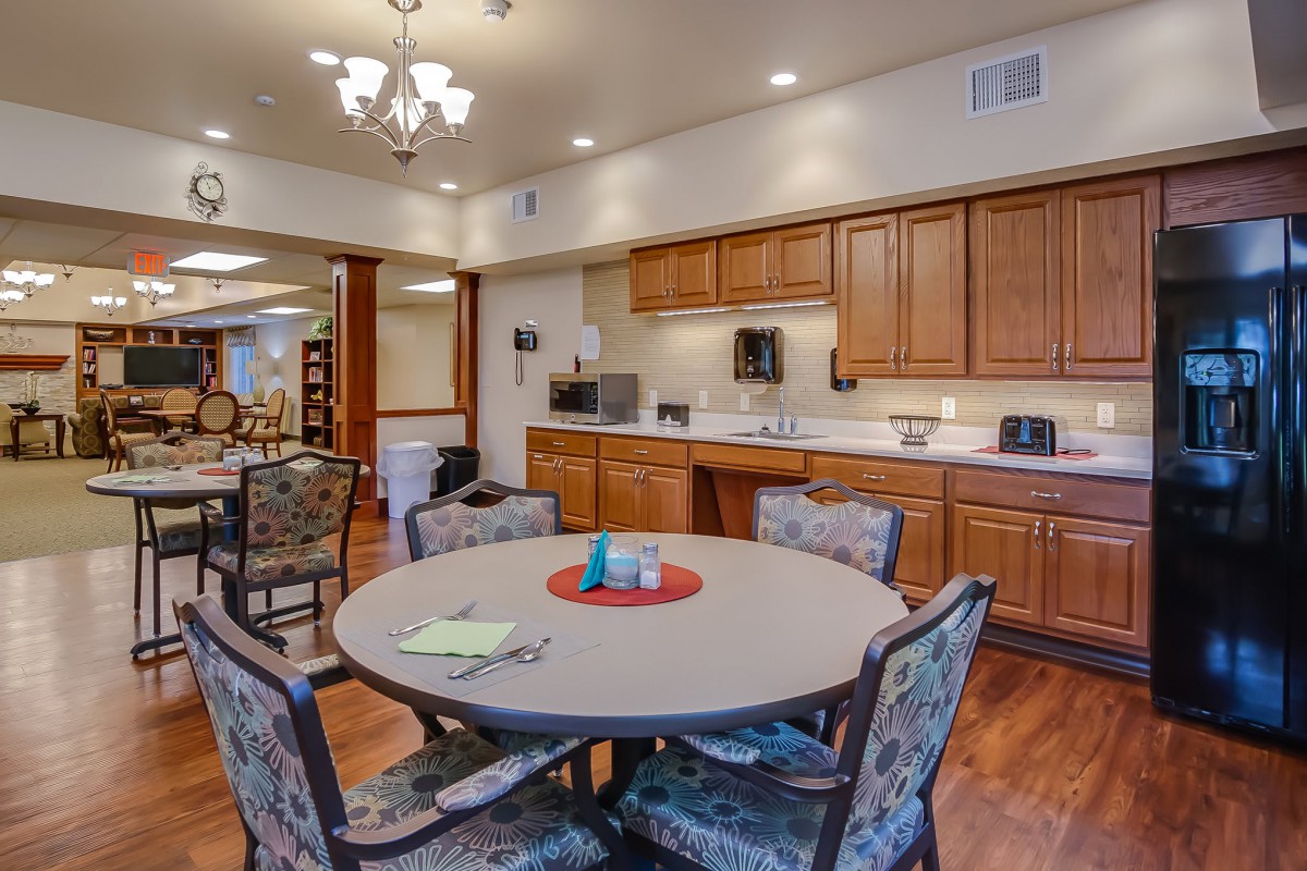 A cozy kitchen and dining area featuring wooden cabinets, a round table with chairs, and a chandelier hanging from the ceiling.