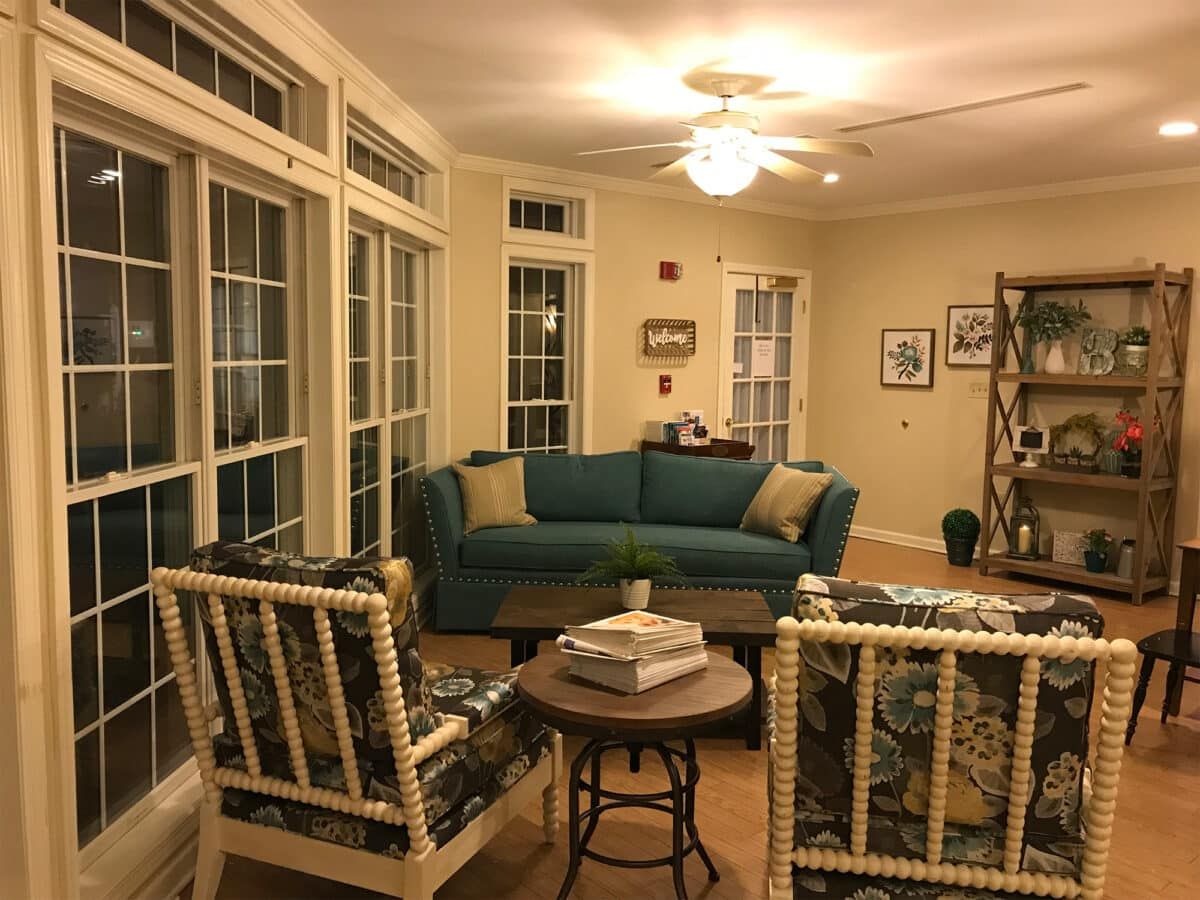 Cozy living room with a teal sofa and patterned chairs, surrounded by large windows.