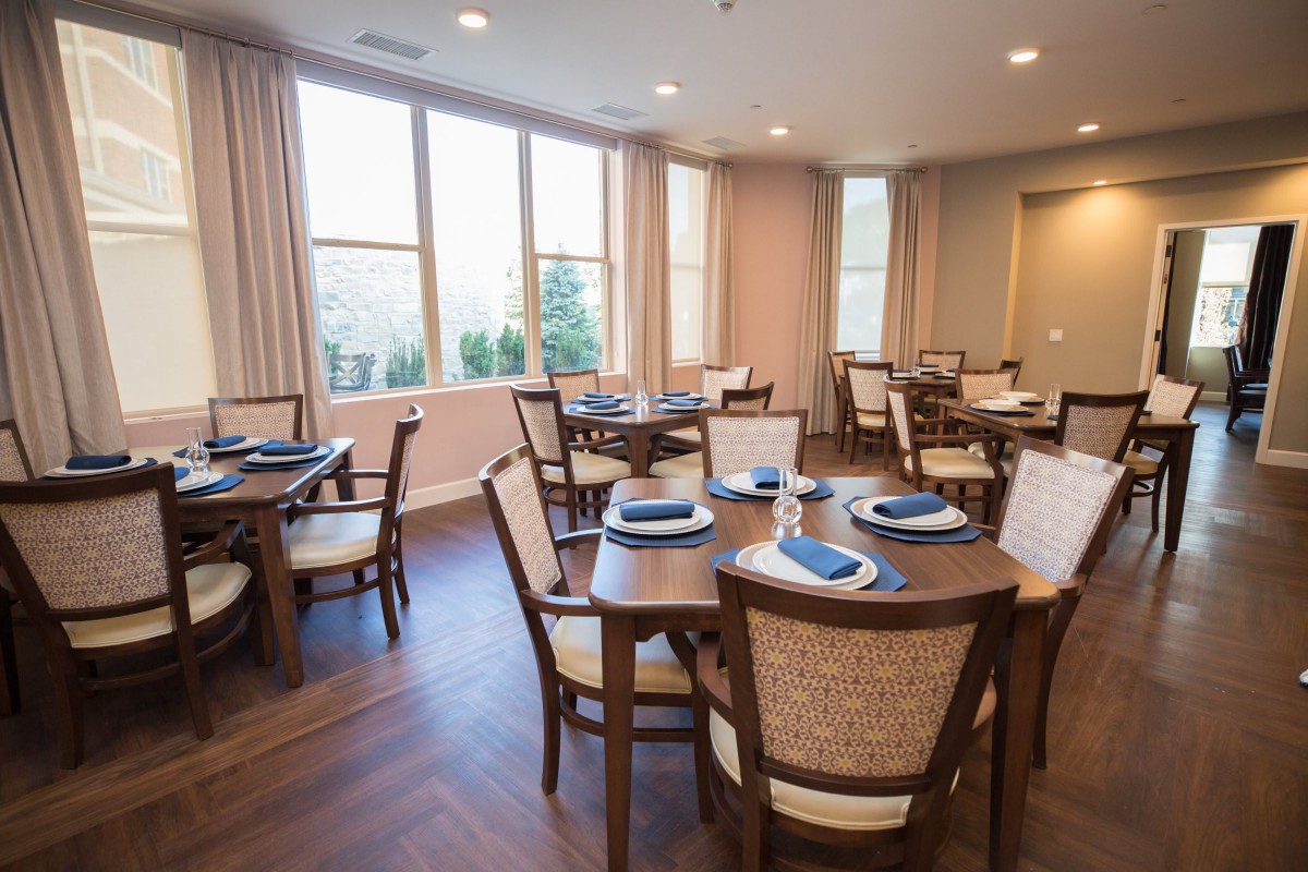 A cozy dining area with neatly arranged tables and chairs, illuminated by natural light coming through the windows.
