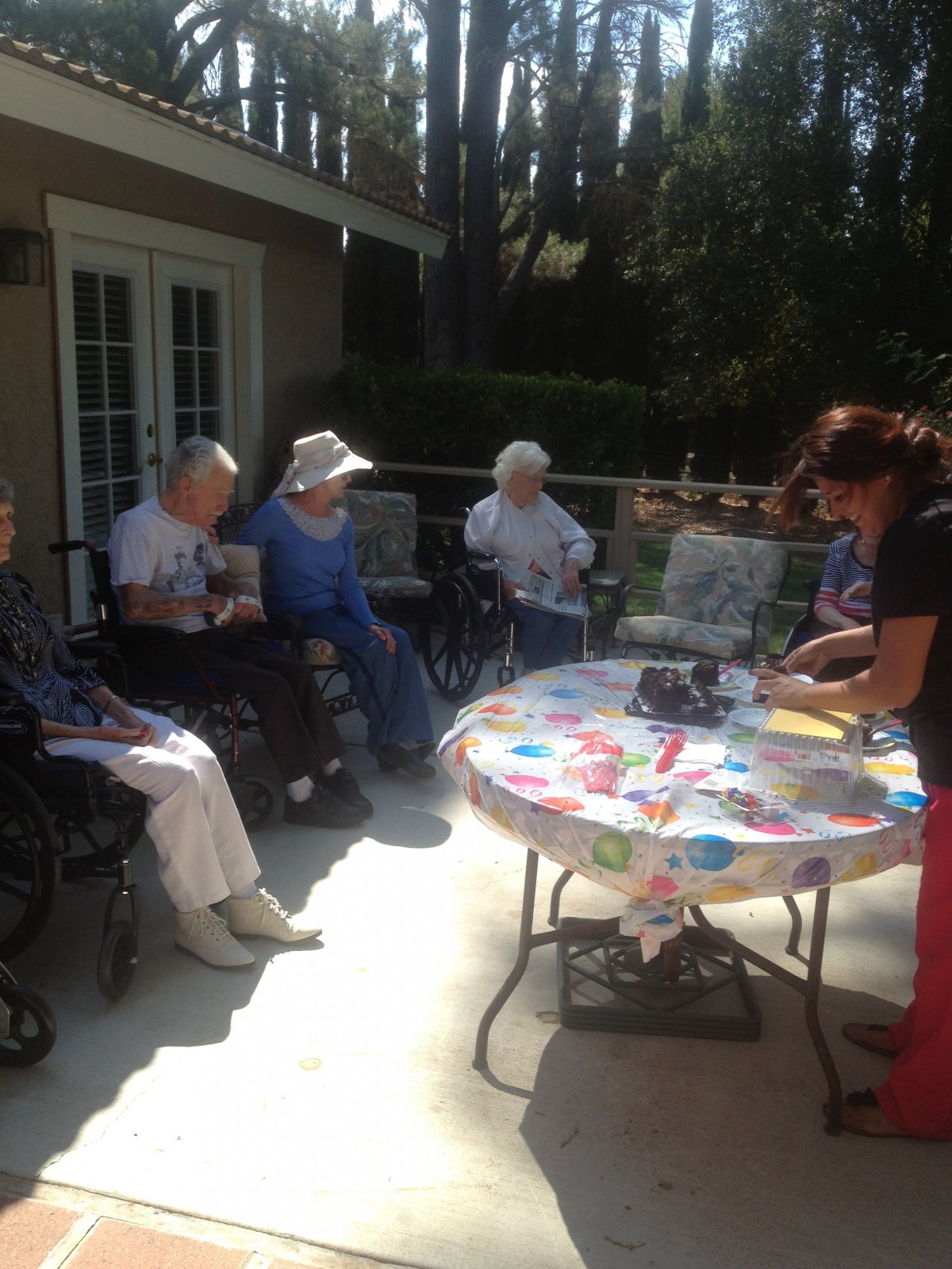A group of elderly people sitting outdoors, enjoying a sunny day together around a table.