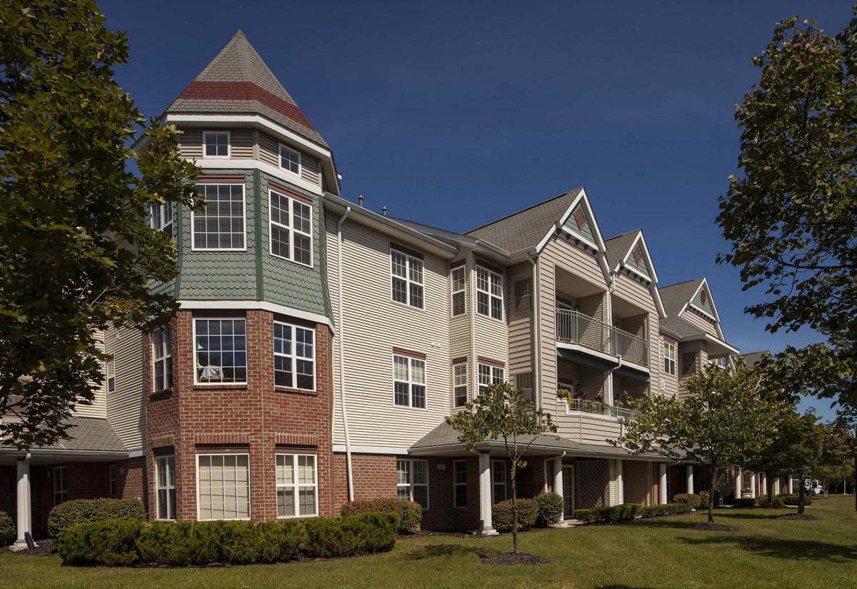 A modern residential apartment building with a mix of brick and siding exterior, featuring multiple balconies and large windows.