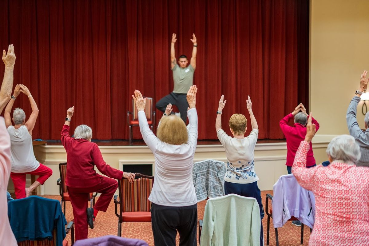 A group of older adults participating in a yoga class indoors, following an instructor.