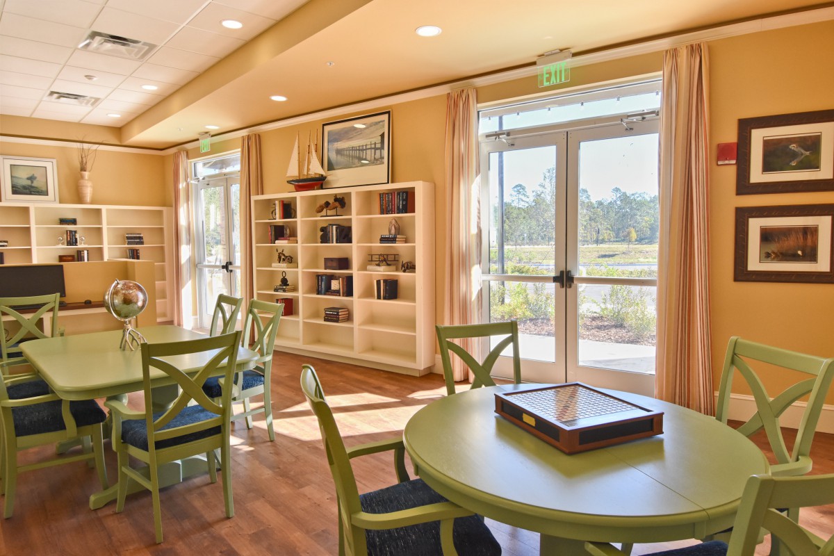 A cozy library interior with bookshelves, tables, and chairs, bathed in natural light streaming through large windows.