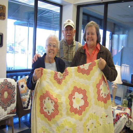 A joyful moment captured as three individuals proudly display a beautiful handmade quilt.