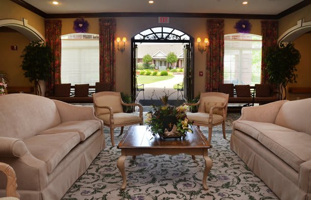 A well-decorated living room with comfortable sofas and chairs arranged around a coffee table, featuring an elegant carpet and an open archway leading to an outdoor view.