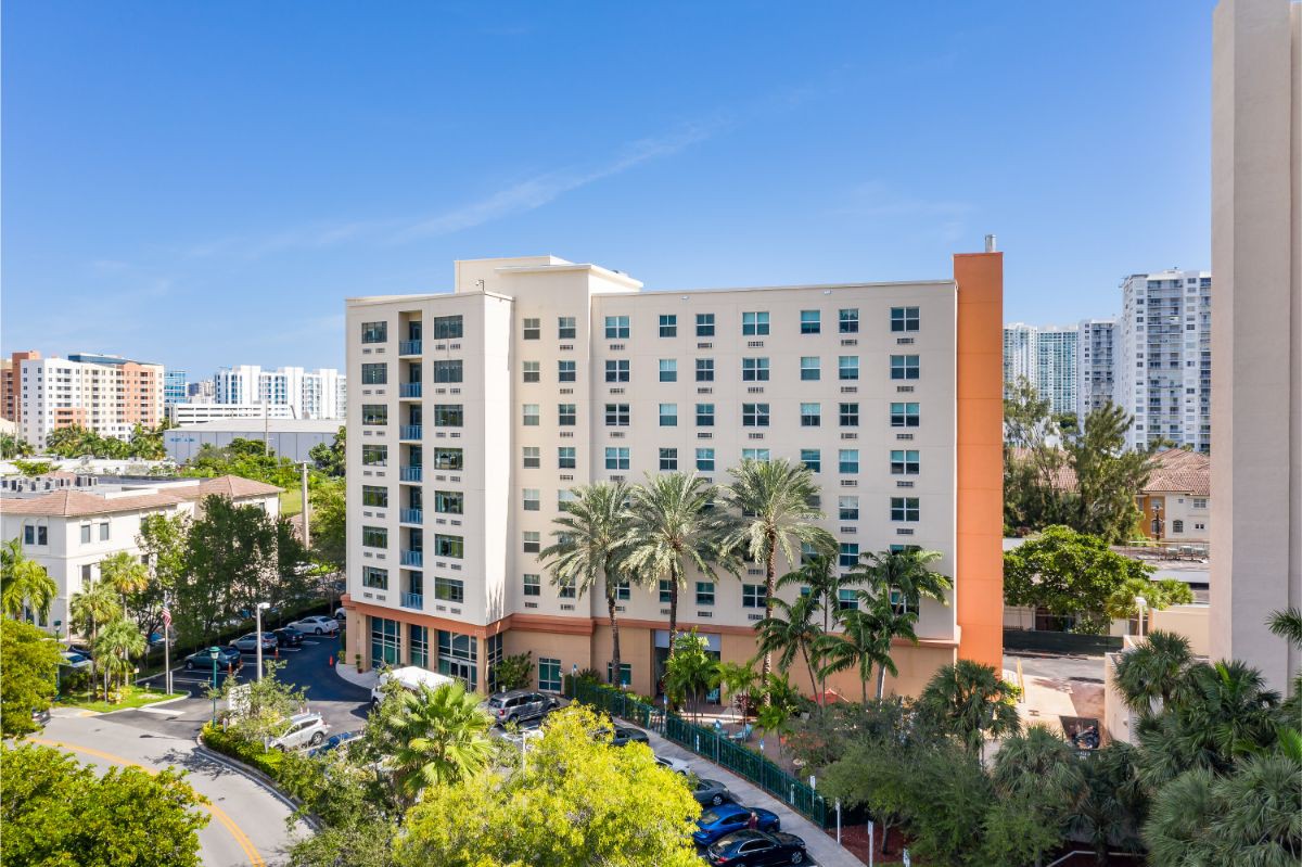 A modern residential apartment building surrounded by palm trees in an urban setting.
