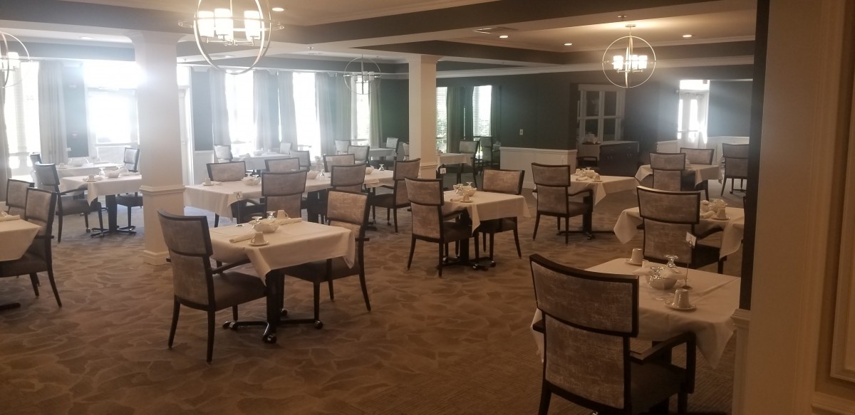 An empty dining room with neatly arranged tables and chairs, featuring elegant lighting.