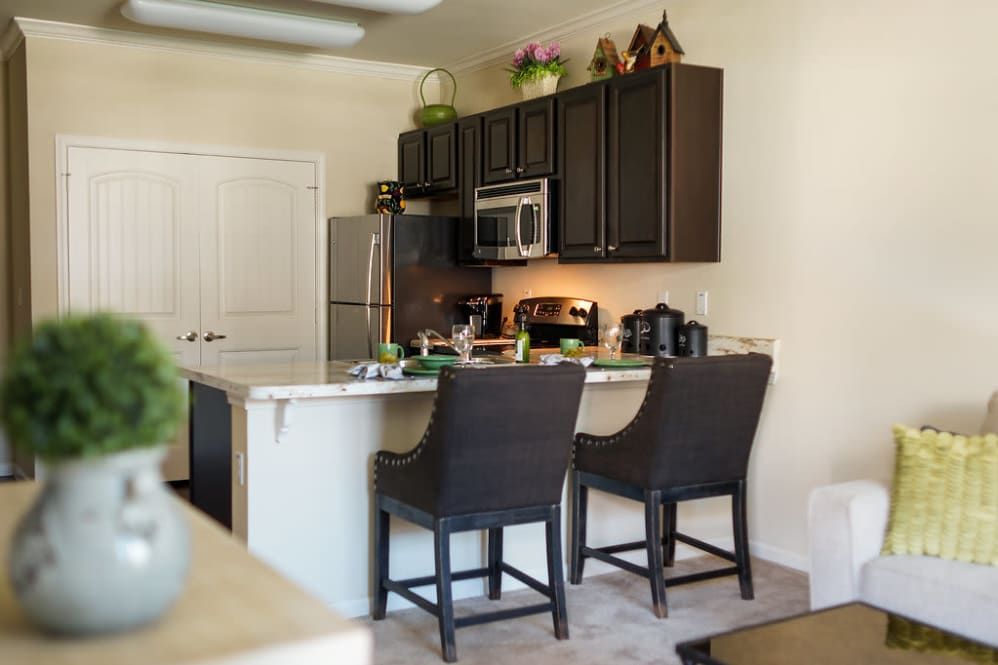 A modern kitchen with dark cabinets, a stainless steel fridge, and bar stools at the counter.