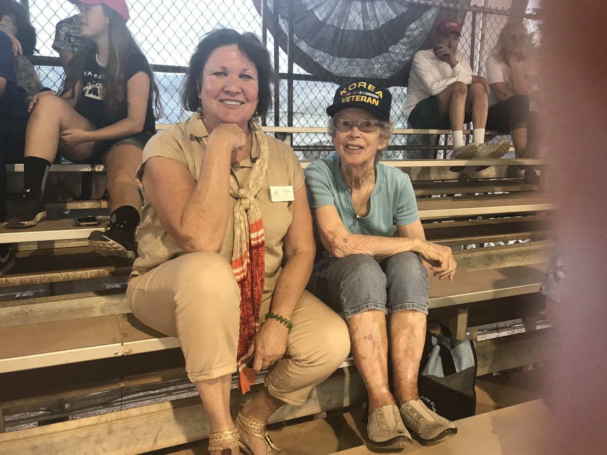 Two women sitting on bleachers, enjoying an outdoor event.
