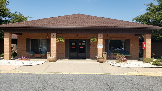A brick building with potted plants flanking the entrance and a parking lot in front.