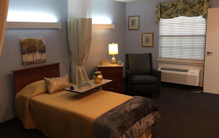 A cozy bedroom with soft lighting, featuring a bed, armchair, and decorative accents.