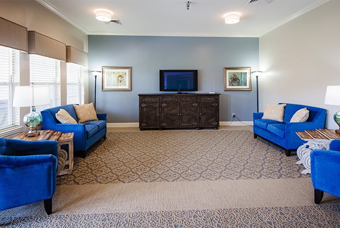 A modern living room with blue sofas, a television on a dark dresser, and decorative lamps and artwork.