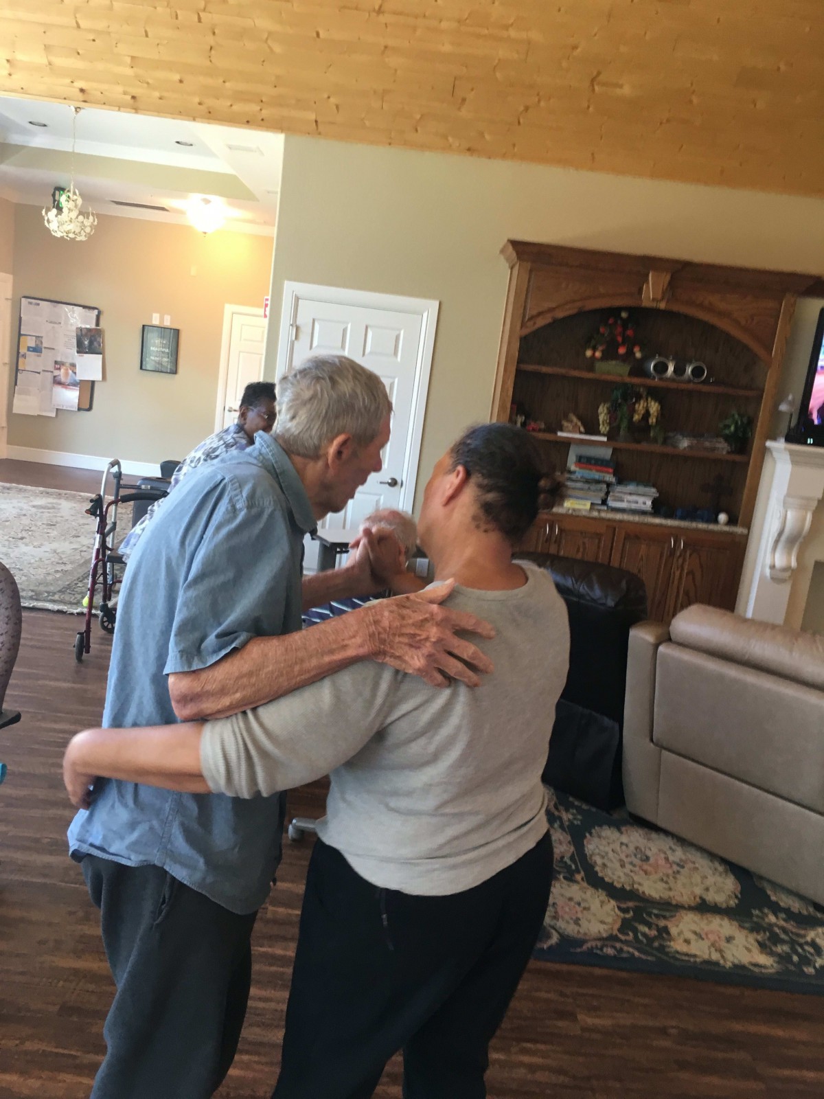 An elderly couple shares a heartfelt dance in a cozy home setting.