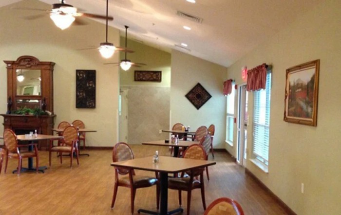 A well-lit dining area with neatly arranged tables and chairs, complemented by decorative wall art and large windows.