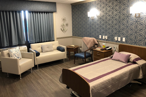 A well-lit and thoughtfully designed hospital patient room featuring a bed, seating area, and modern decor.