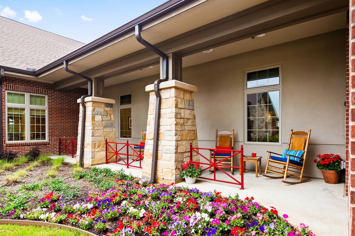 A cozy outdoor porch with chairs and a vibrant garden filled with colorful flowers.